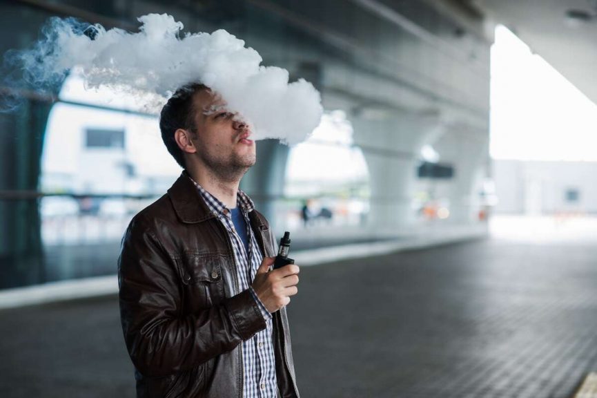 男子吸电子烟在侧面对机场航站楼的背景